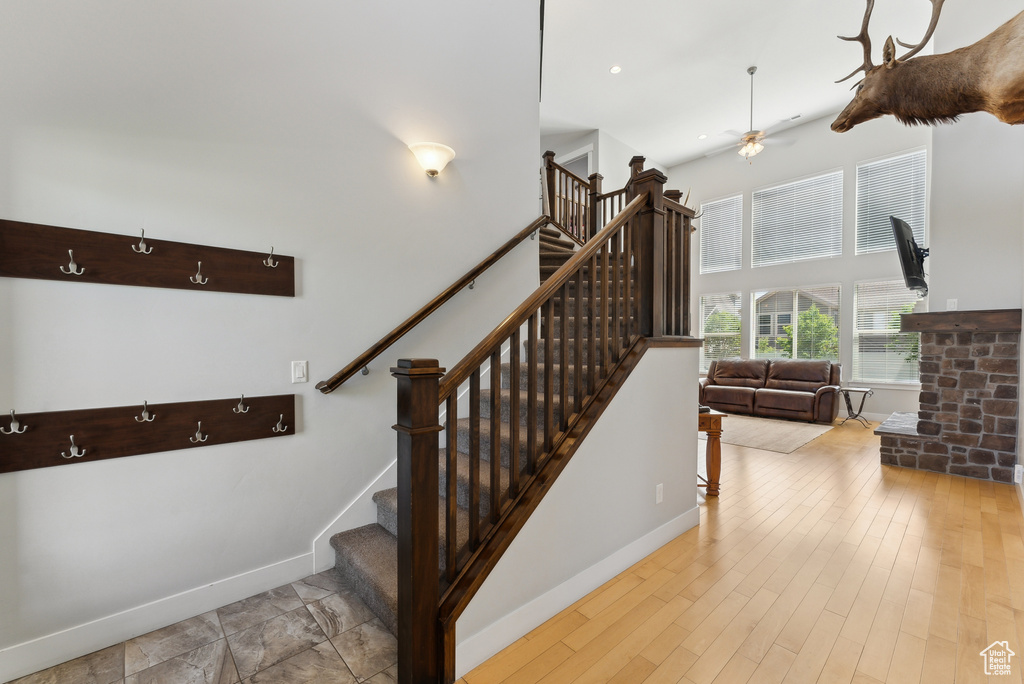 Staircase featuring ceiling fan, a high ceiling, baseboards, and wood finished floors
