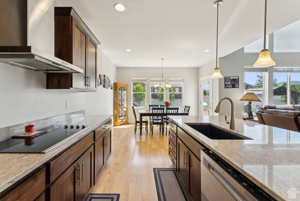 Kitchen featuring wall chimney exhaust hood, a sink, dishwasher, hanging light fixtures, and recessed lighting