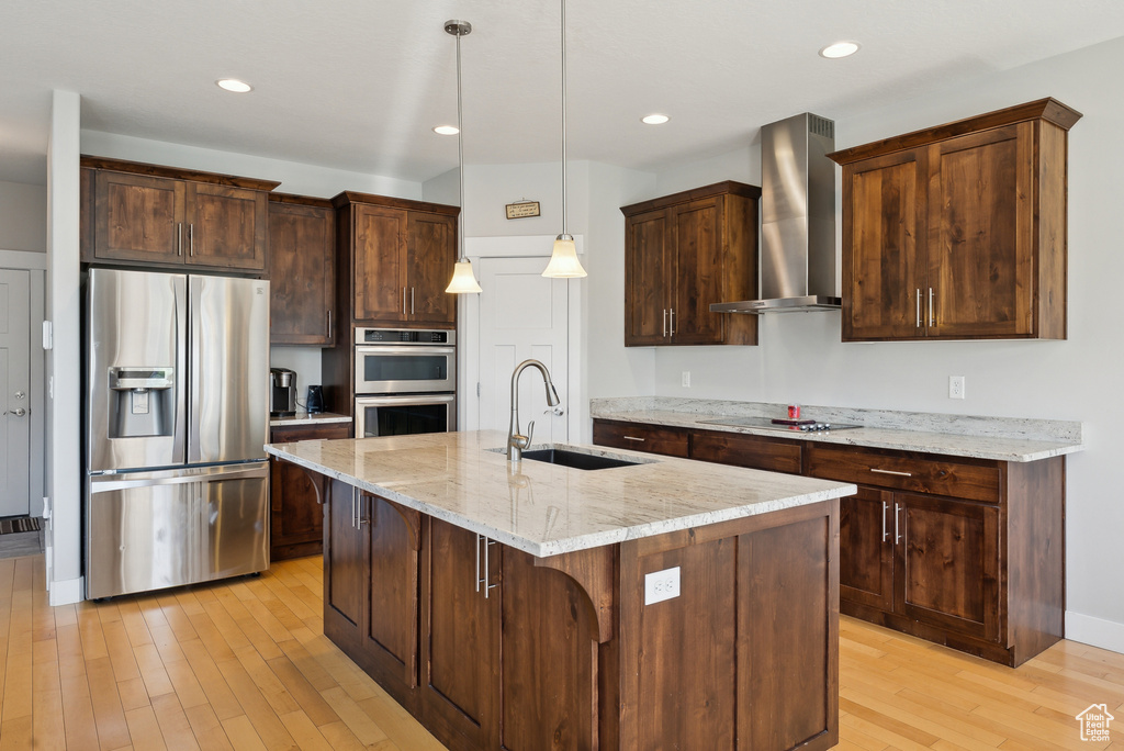 Kitchen featuring stainless steel appliances, wall chimney range hood, a sink, light wood-style floors, and light stone counters