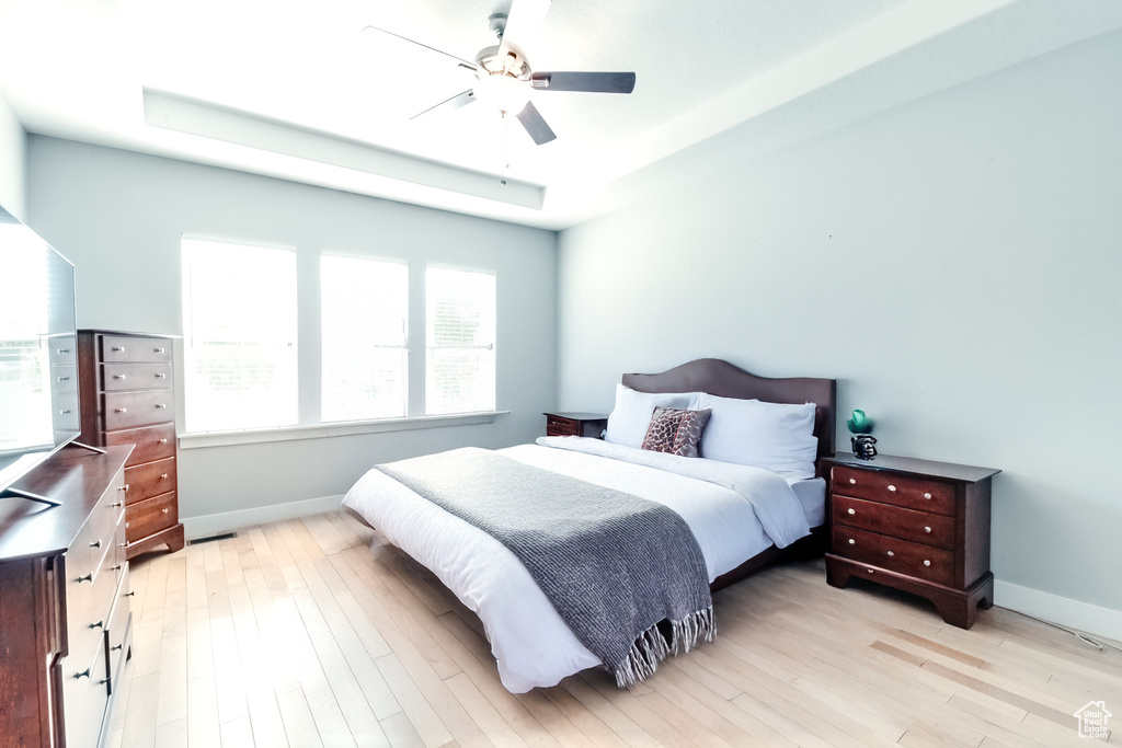 Bedroom featuring a raised ceiling, baseboards, light wood-type flooring, and ceiling fan