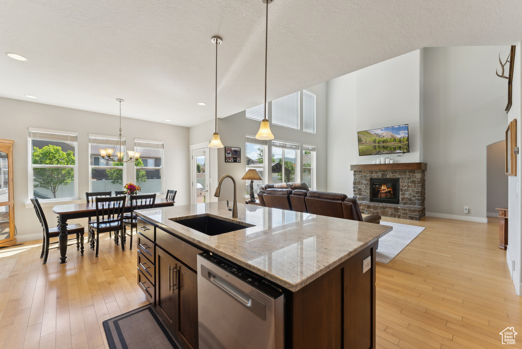 Kitchen featuring a sink, dishwasher, a stone fireplace, dark brown cabinets, and recessed lighting
