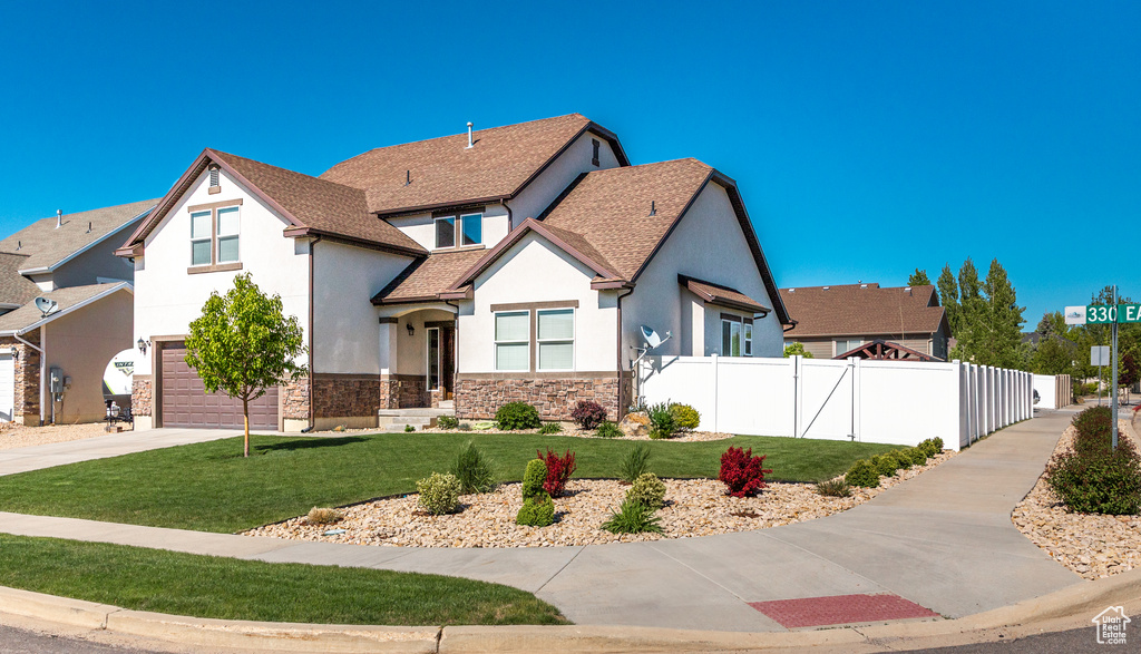 View of front of house with stucco siding, an attached garage, driveway, stone siding, and a shingled roof