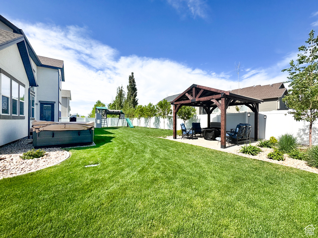 View of yard featuring a hot tub, a gazebo, a patio area, a playground, and an outdoor living space