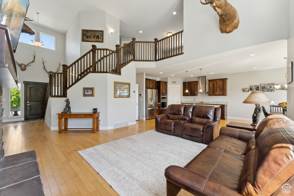 Living area featuring a high ceiling, stairs, light wood finished floors, baseboards, and recessed lighting