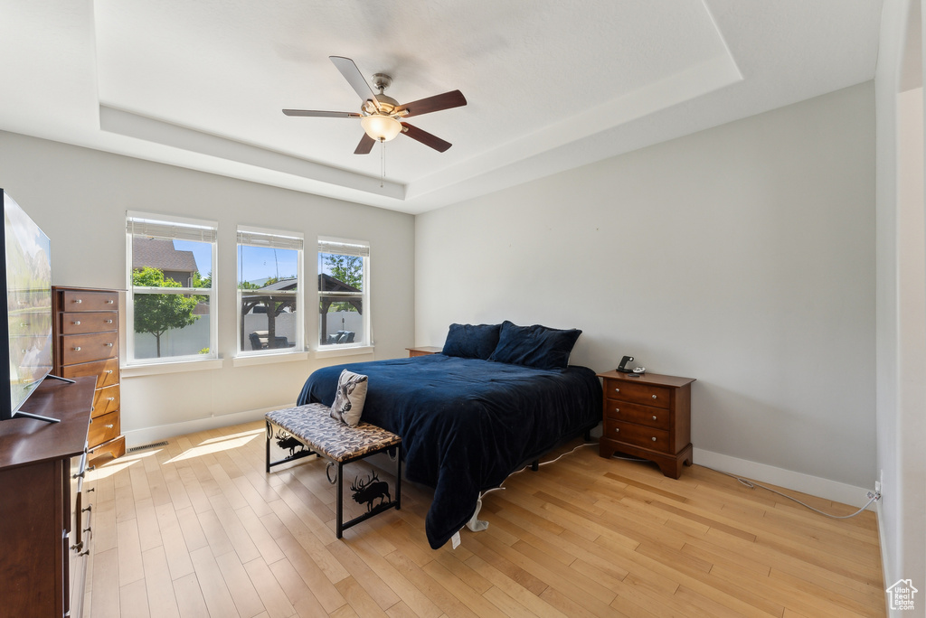 Bedroom with a tray ceiling, baseboards, light wood-type flooring, and a ceiling fan