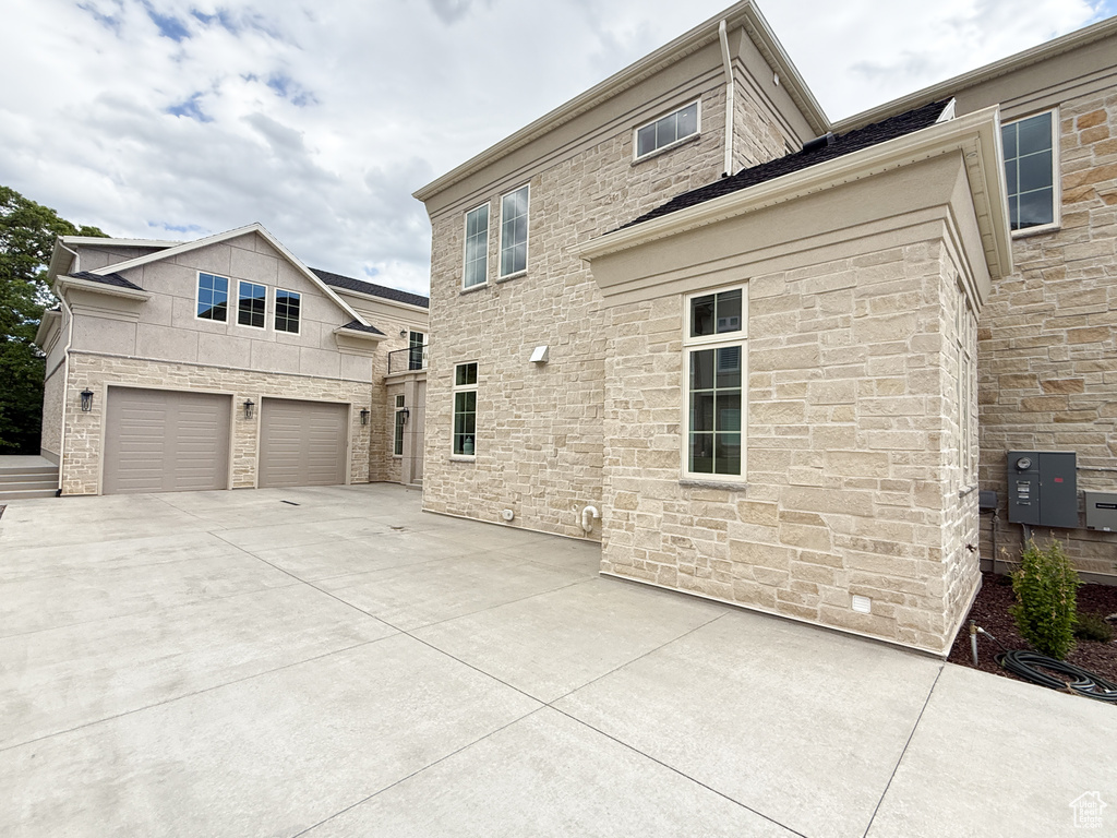 Back of property with stone siding, a garage, and concrete driveway