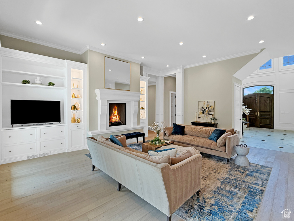 Living room featuring light wood-style floors, a warm lit fireplace, recessed lighting, crown molding, and built in shelves
