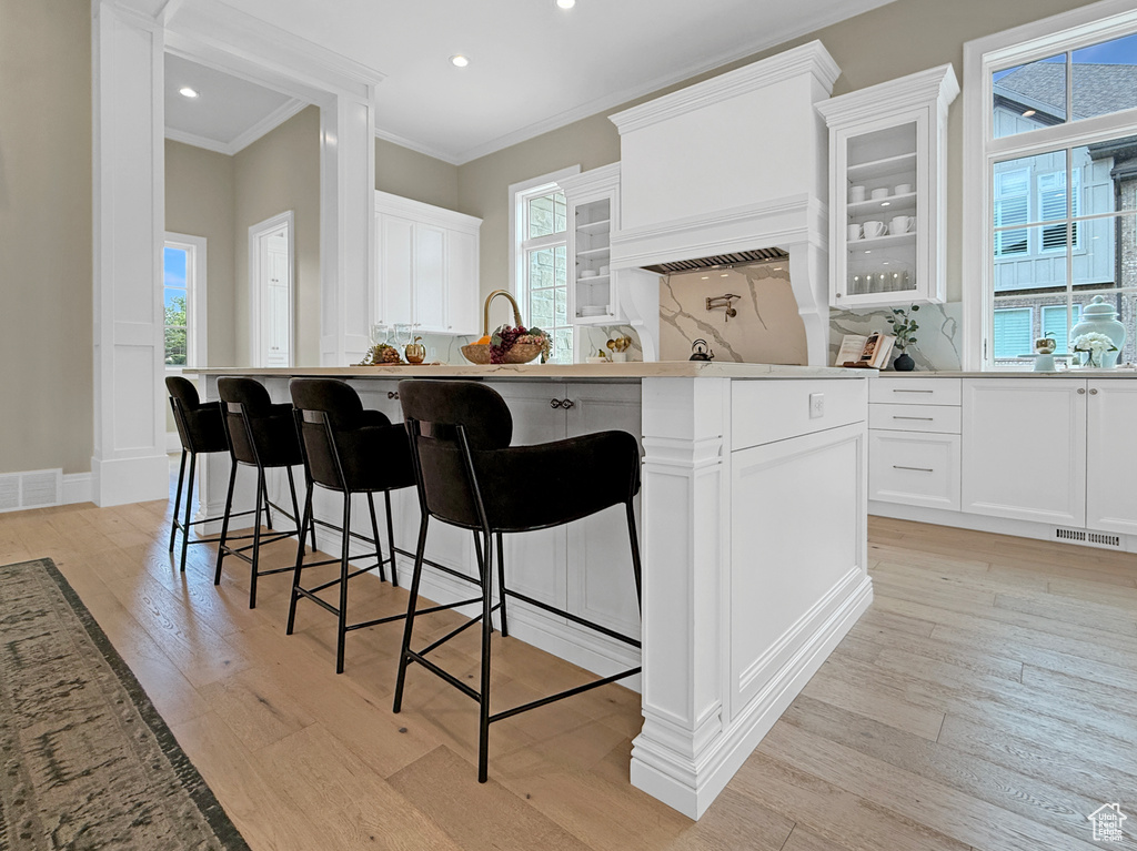 Kitchen with ornamental molding, light wood-type flooring, backsplash, glass insert cabinets, and white cabinetry