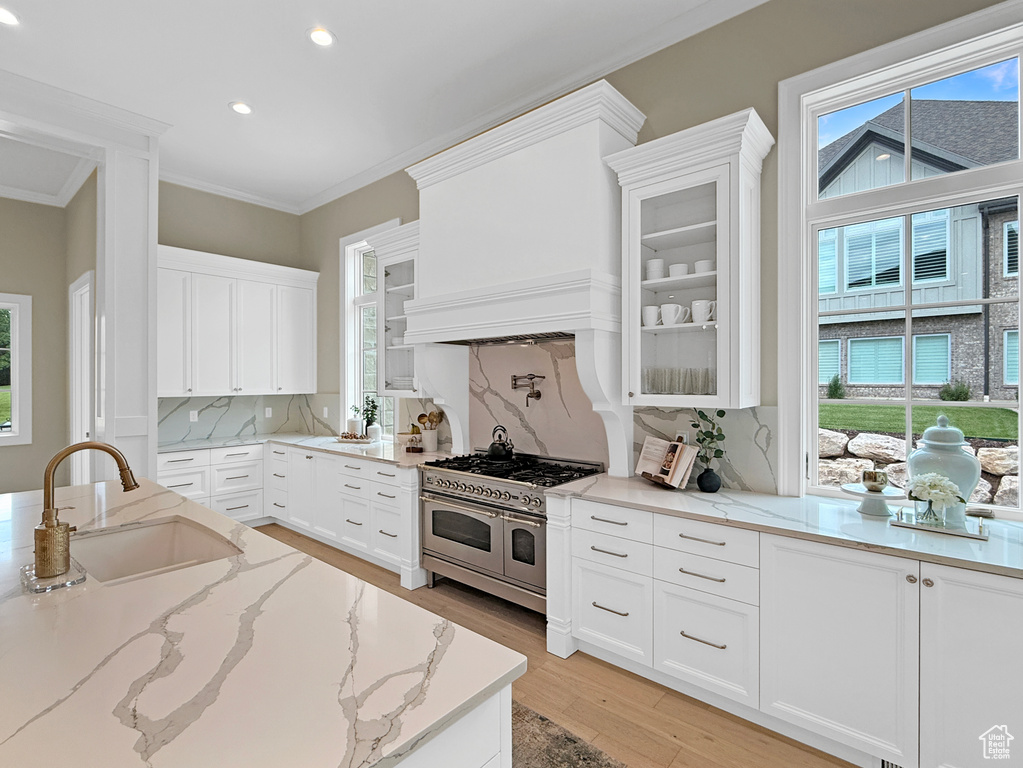 Kitchen with a sink, range with two ovens, recessed lighting, glass insert cabinets, and ornamental molding