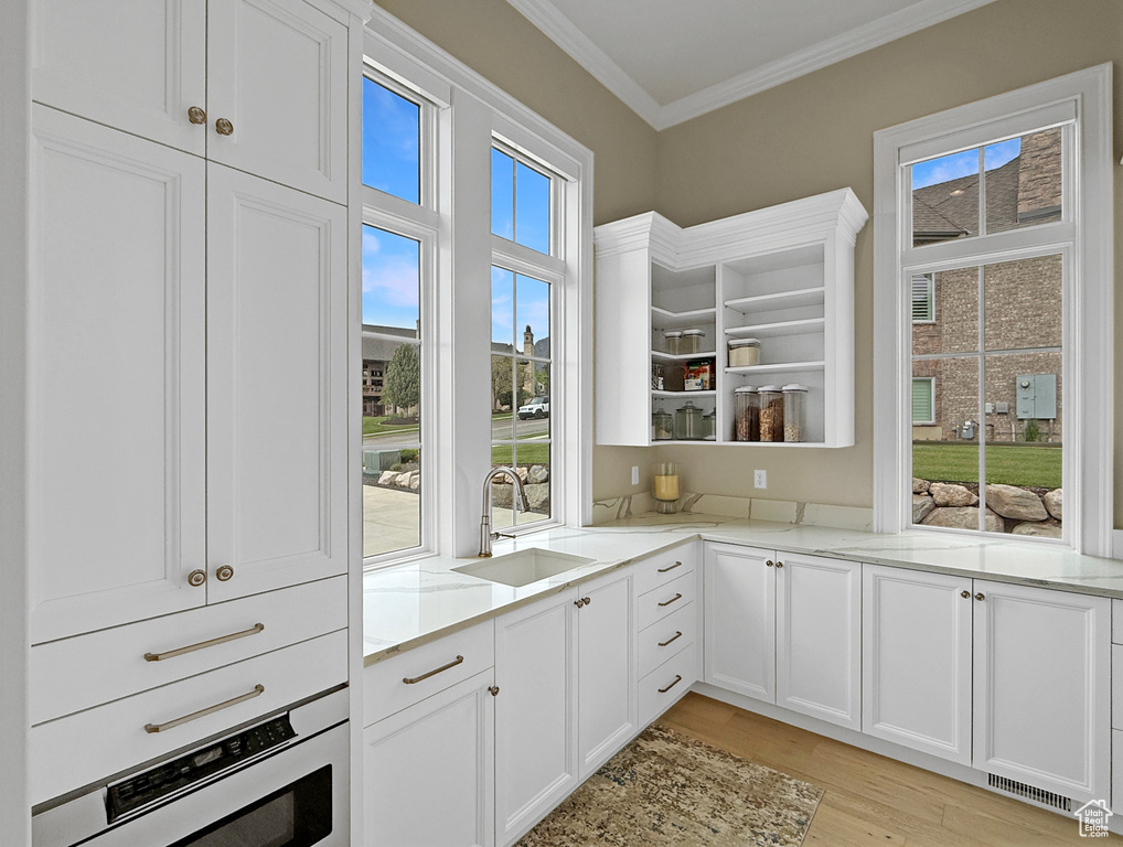 Kitchen with a sink, oven, crown molding, open shelves, and light wood finished floors