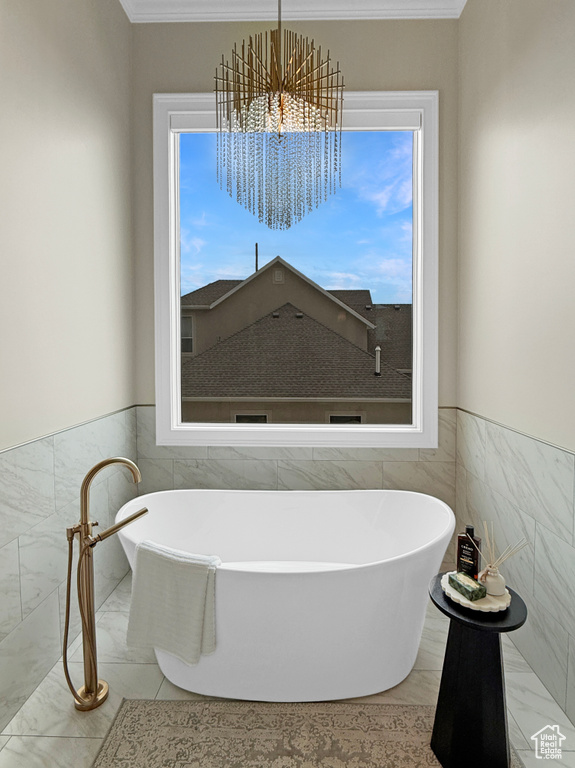 Full bath with tile walls, a soaking tub, marble finish floors, a chandelier, and crown molding
