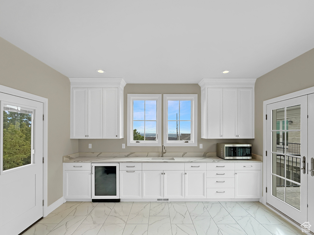 Kitchen with beverage cooler, stainless steel microwave, light marble finish flooring, a sink, and plenty of natural light