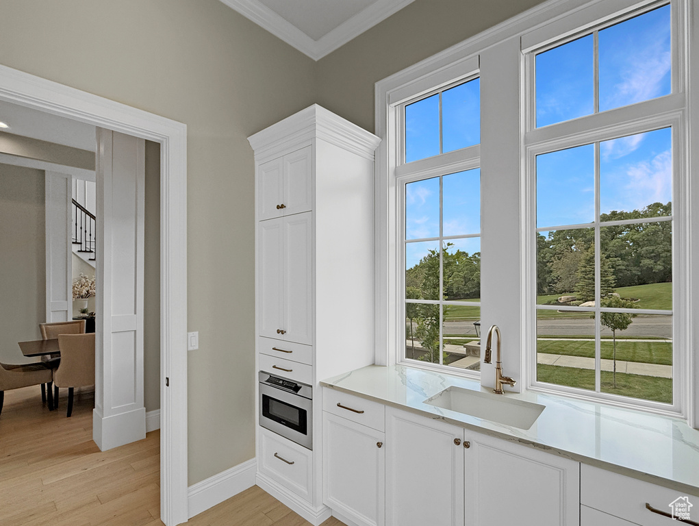 Kitchen with a sink, oven, ornamental molding, light wood-style floors, and healthy amount of natural light