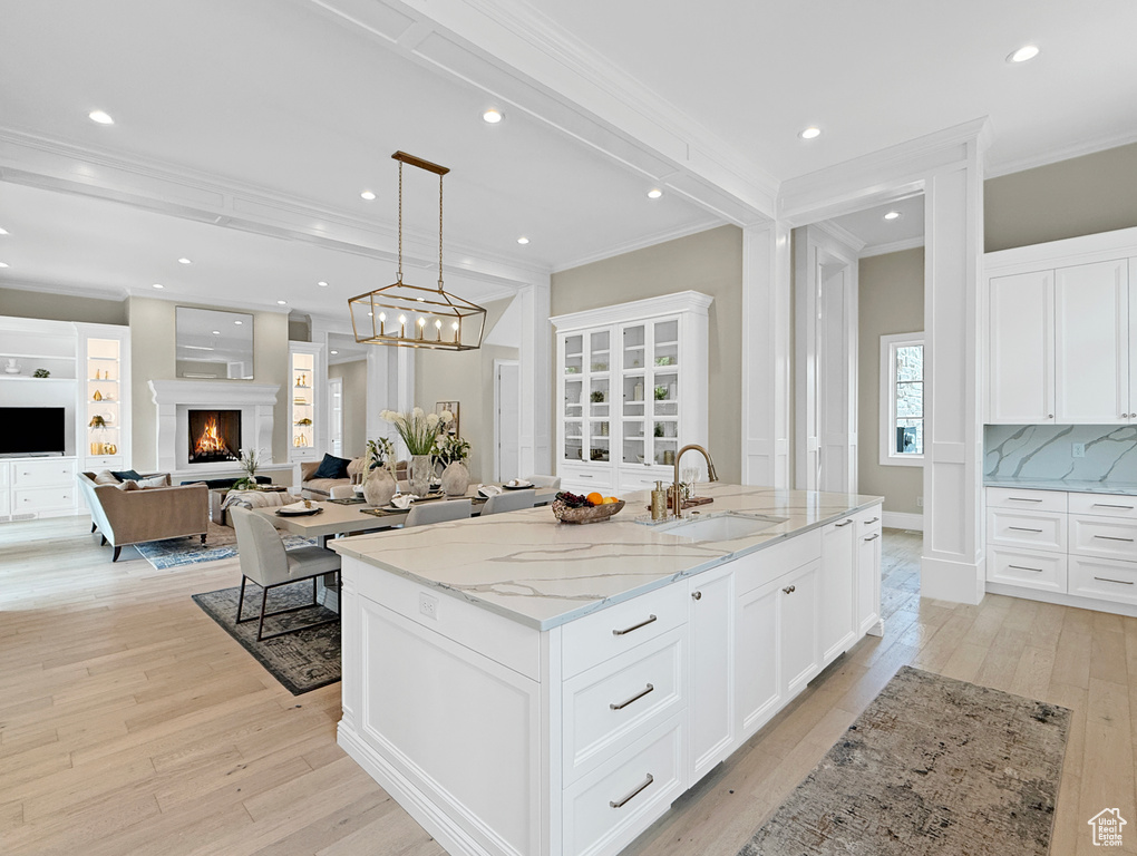 Kitchen featuring crown molding, light wood-type flooring, a center island with sink, a sink, and white cabinetry