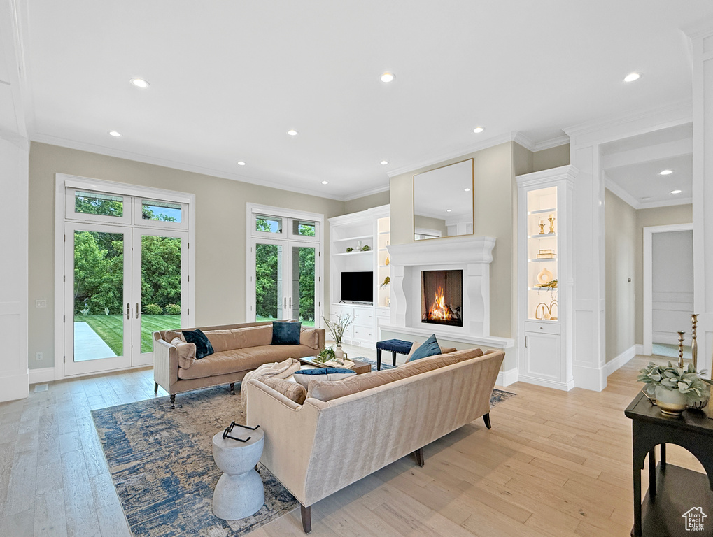 Living room featuring french doors, light wood-style floors, crown molding, a warm lit fireplace, and recessed lighting