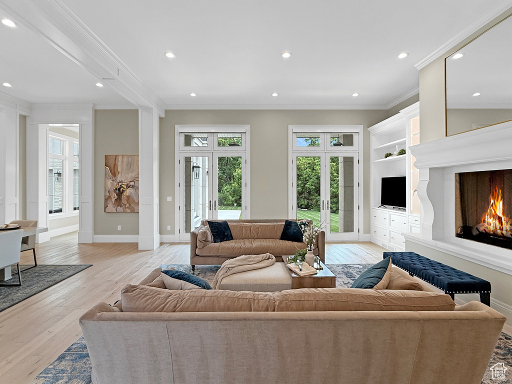 Living room featuring french doors, crown molding, a lit fireplace, light wood-style floors, and recessed lighting