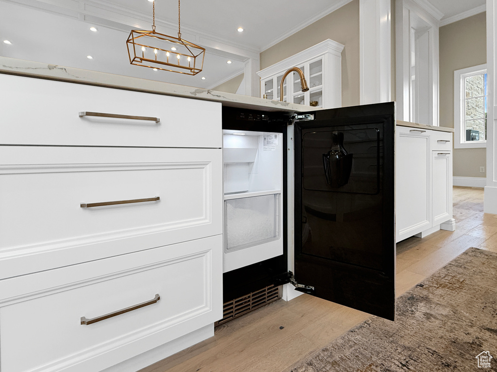 Kitchen view of ornamental molding, light wood-type flooring, white cabinets, decorative light fixtures, and a chandelier