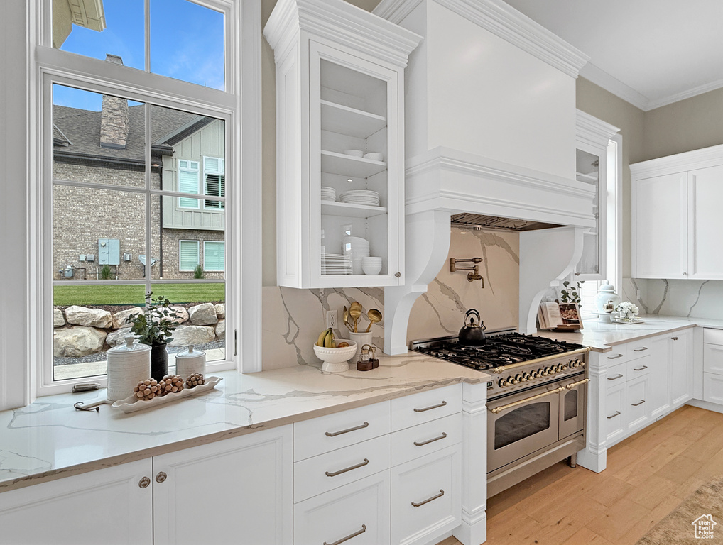 Kitchen with double oven range, white cabinets, light wood-style floors, glass insert cabinets, and ornamental molding