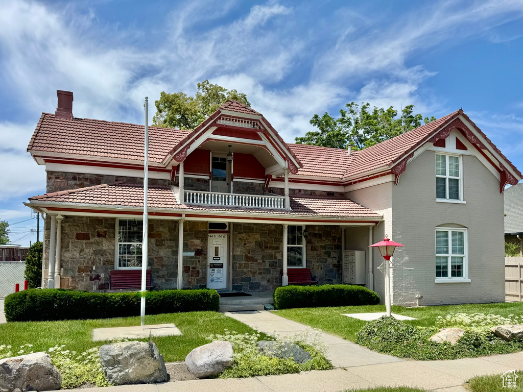 View of front of property featuring a tiled roof, a balcony, a porch, and a chimney