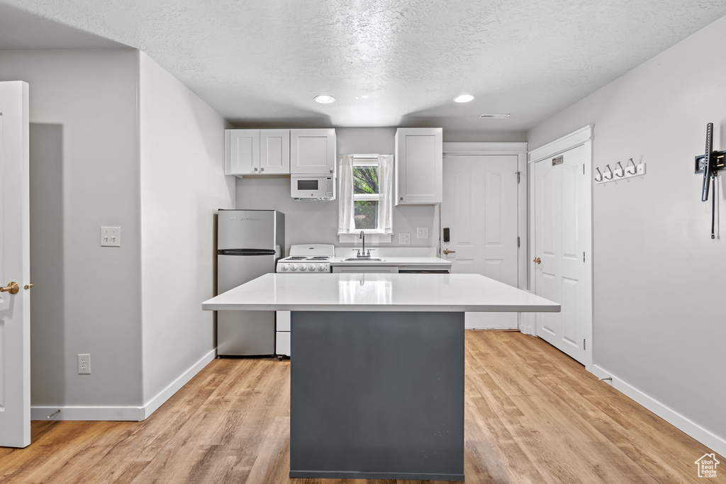 Kitchen with light countertops, a center island, a textured ceiling, baseboards, and white appliances