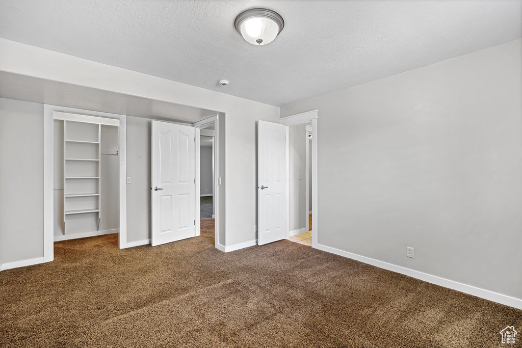 Unfurnished bedroom with carpet floors, baseboards, a closet, and a textured ceiling
