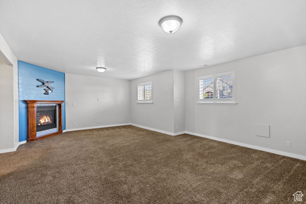 Unfurnished living room with carpet flooring, a glass covered fireplace, baseboards, and a textured ceiling