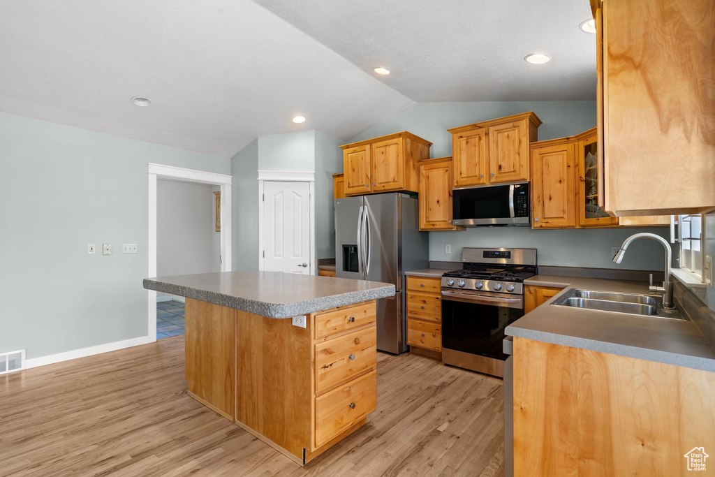 Kitchen with appliances with stainless steel finishes, a sink, lofted ceiling, a center island, and light wood-style flooring