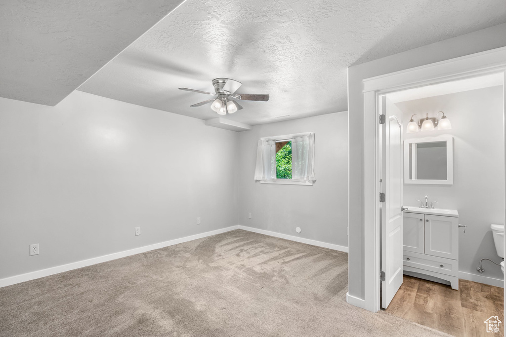 Unfurnished bedroom featuring baseboards, a textured ceiling, light colored carpet, ensuite bathroom, and a sink