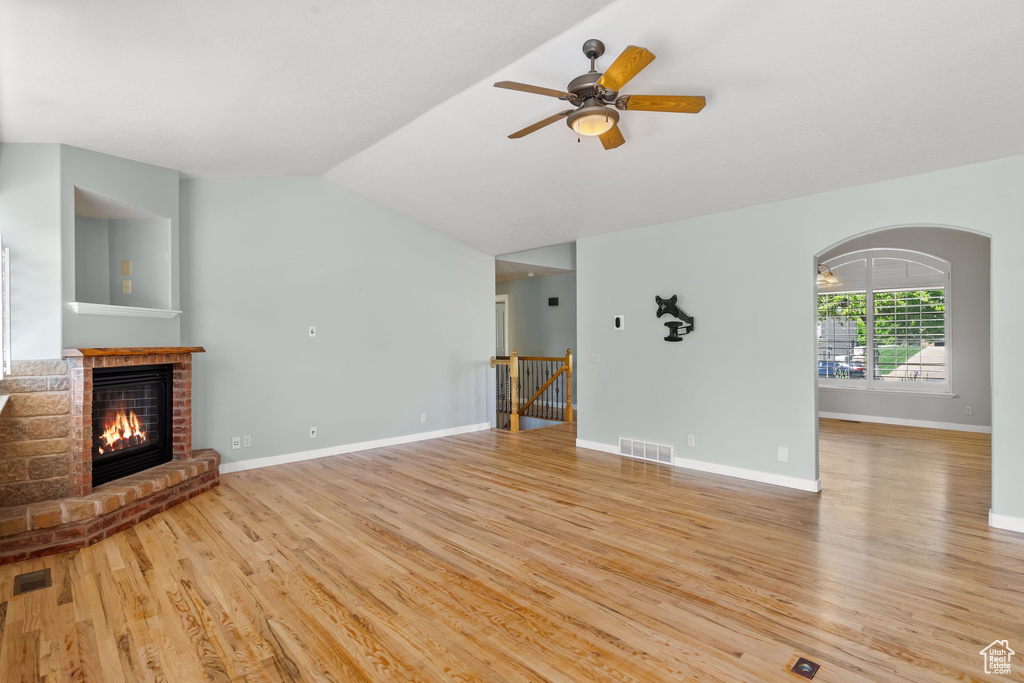 Unfurnished living room featuring light wood finished floors, a brick fireplace, a ceiling fan, lofted ceiling, and baseboards