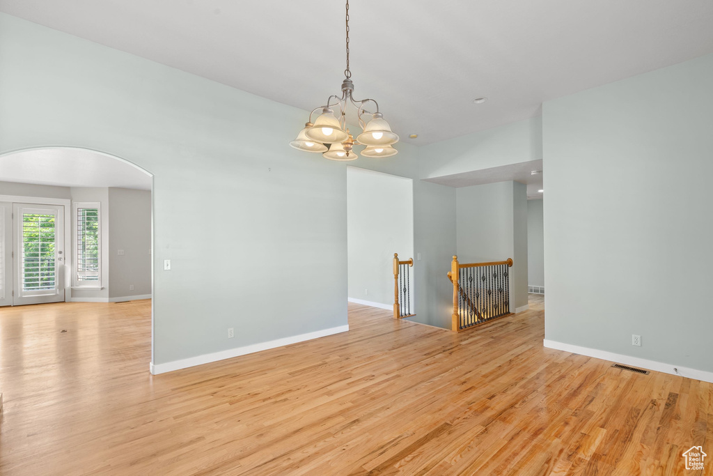 Empty room featuring arched walkways, light wood finished floors, a chandelier, and baseboards