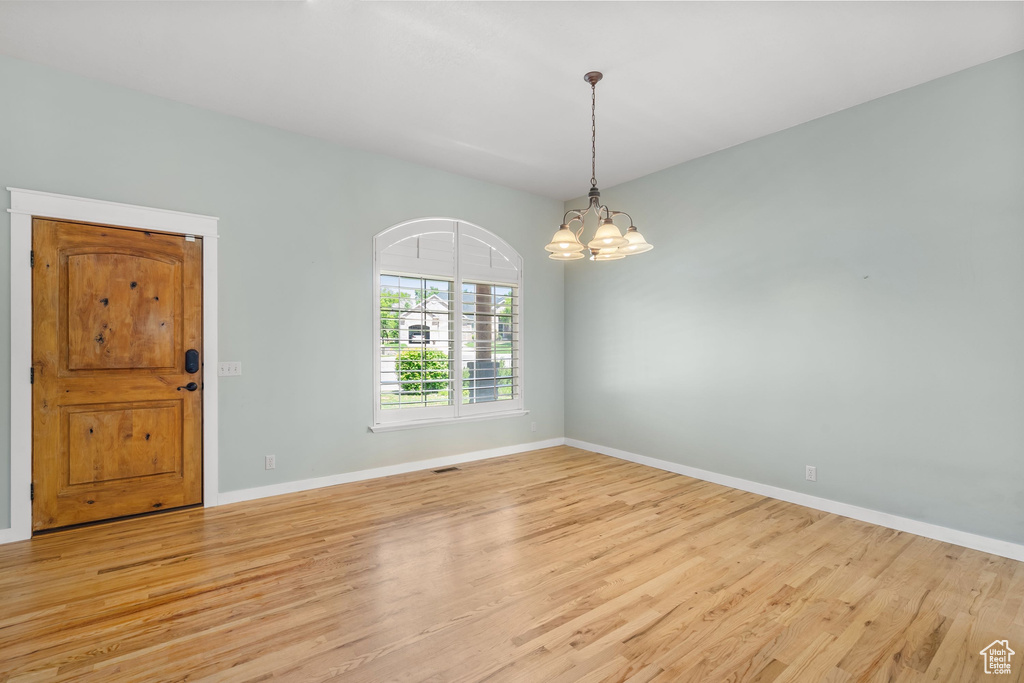 Empty room featuring light wood finished floors, baseboards, and a chandelier