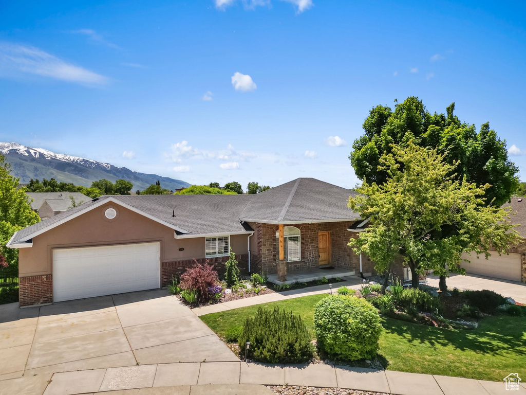 Single story home with brick siding, a garage, driveway, a front lawn, and a mountain view