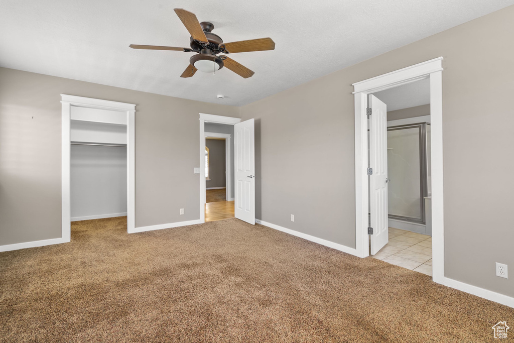 Unfurnished bedroom featuring light colored carpet, a walk in closet, baseboards, and ensuite bathroom