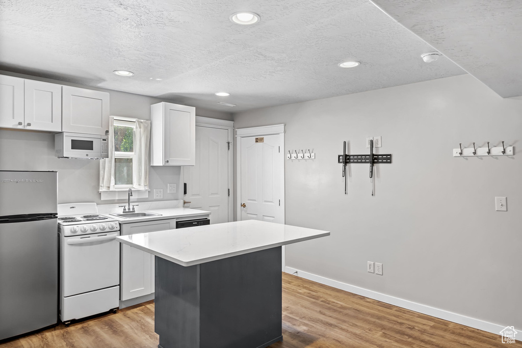 Kitchen featuring white appliances, a sink, light countertops, a kitchen island, and a textured ceiling