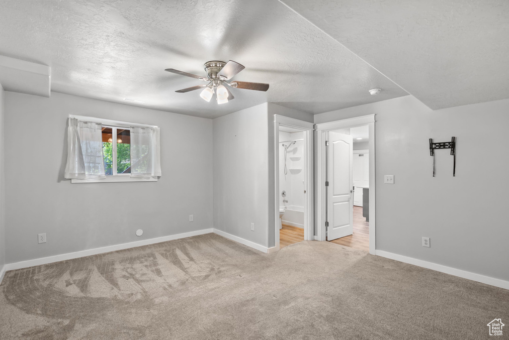Unfurnished bedroom with carpet floors, a textured ceiling, baseboards, connected bathroom, and a ceiling fan