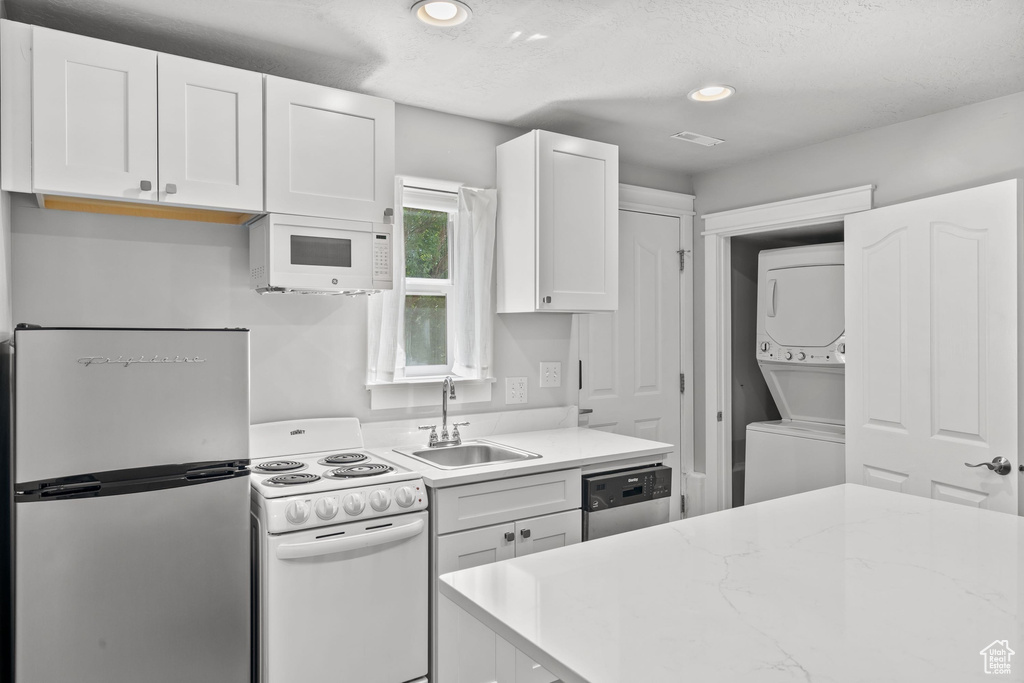 Kitchen with stainless steel appliances, stacked washer / dryer, a sink, white cabinetry, and recessed lighting