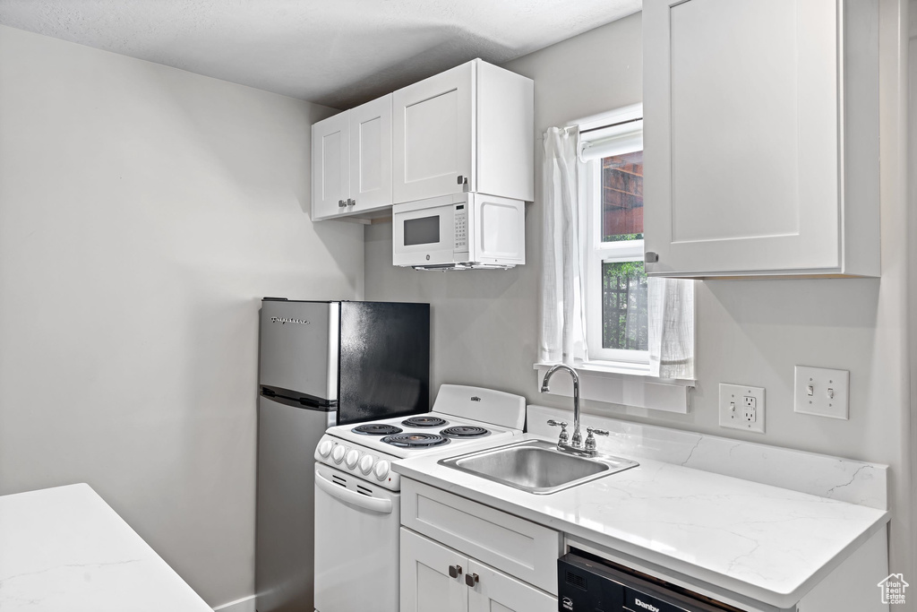 Kitchen featuring white appliances, a sink, and white cabinetry