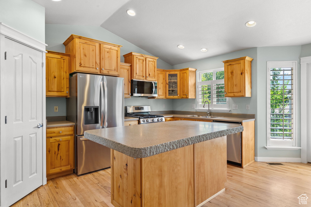 Kitchen featuring appliances with stainless steel finishes, lofted ceiling, light wood-style floors, a sink, and a kitchen island