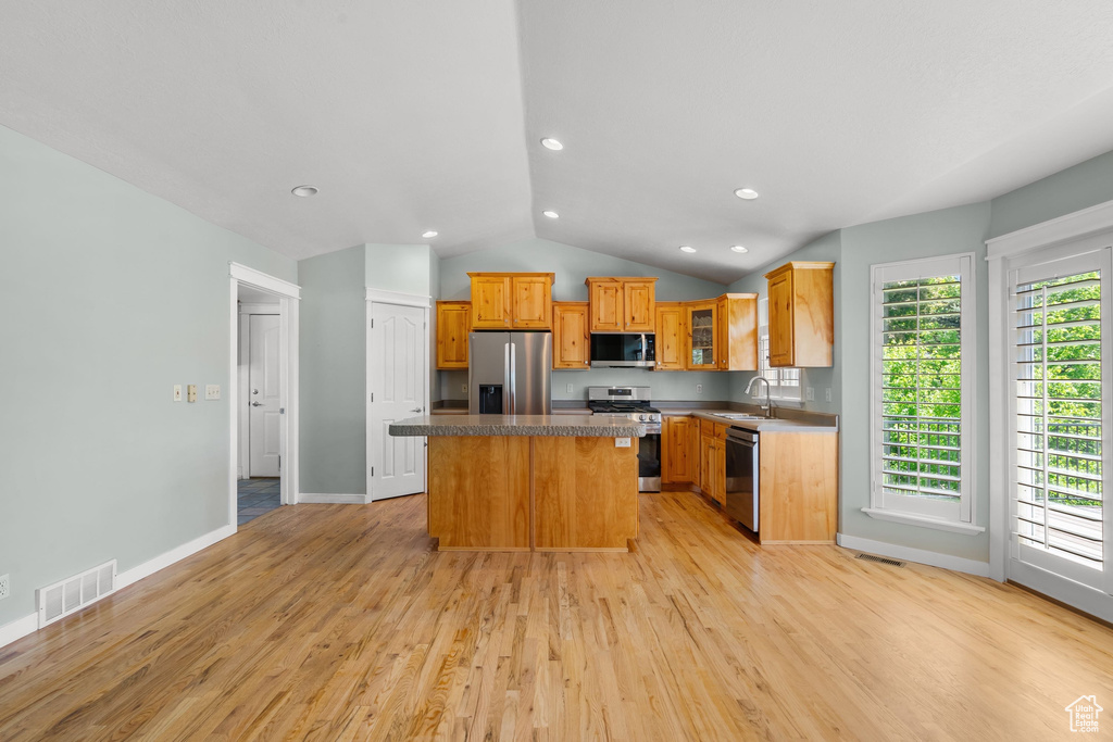 Kitchen featuring appliances with stainless steel finishes, a sink, a center island, lofted ceiling, and light wood-style flooring