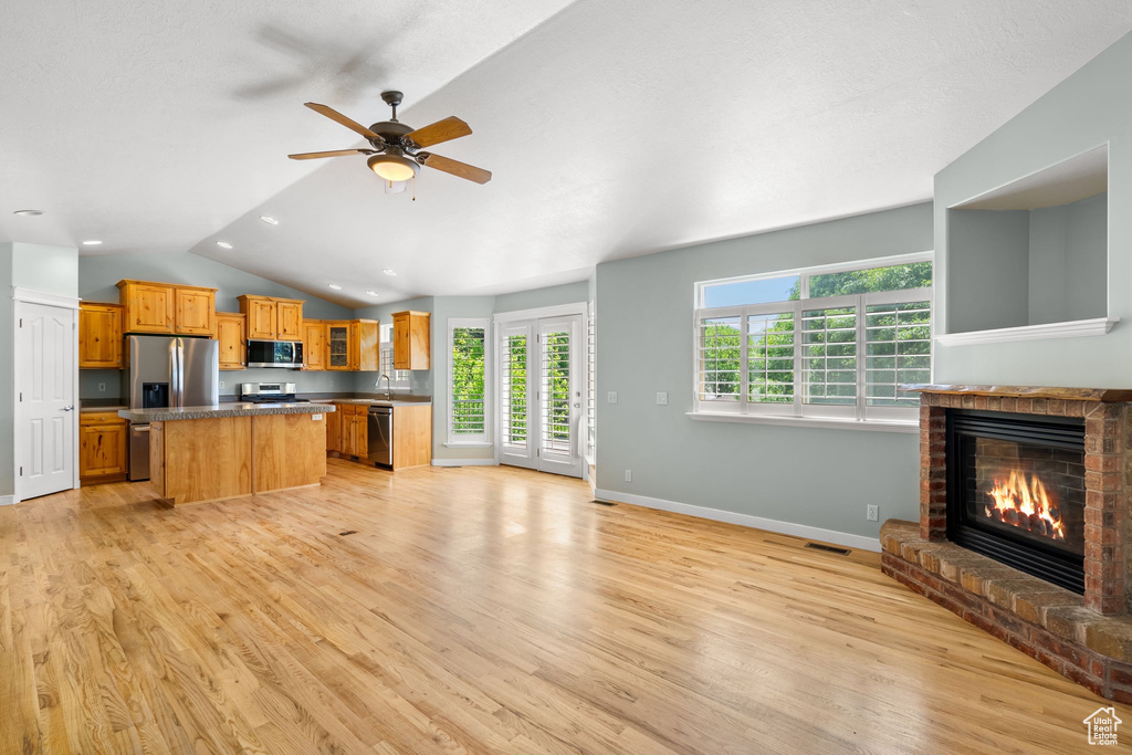 Kitchen featuring appliances with stainless steel finishes, a kitchen island, light wood-style flooring, open floor plan, and lofted ceiling