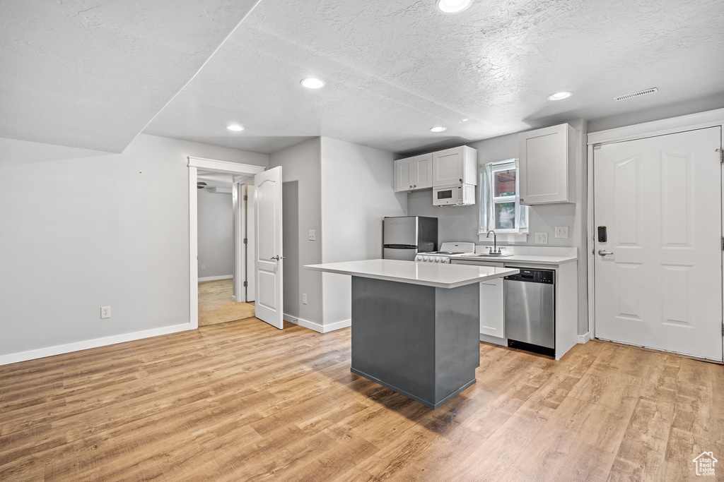 Kitchen with stainless steel appliances, light wood-type flooring, a sink, light countertops, and baseboards