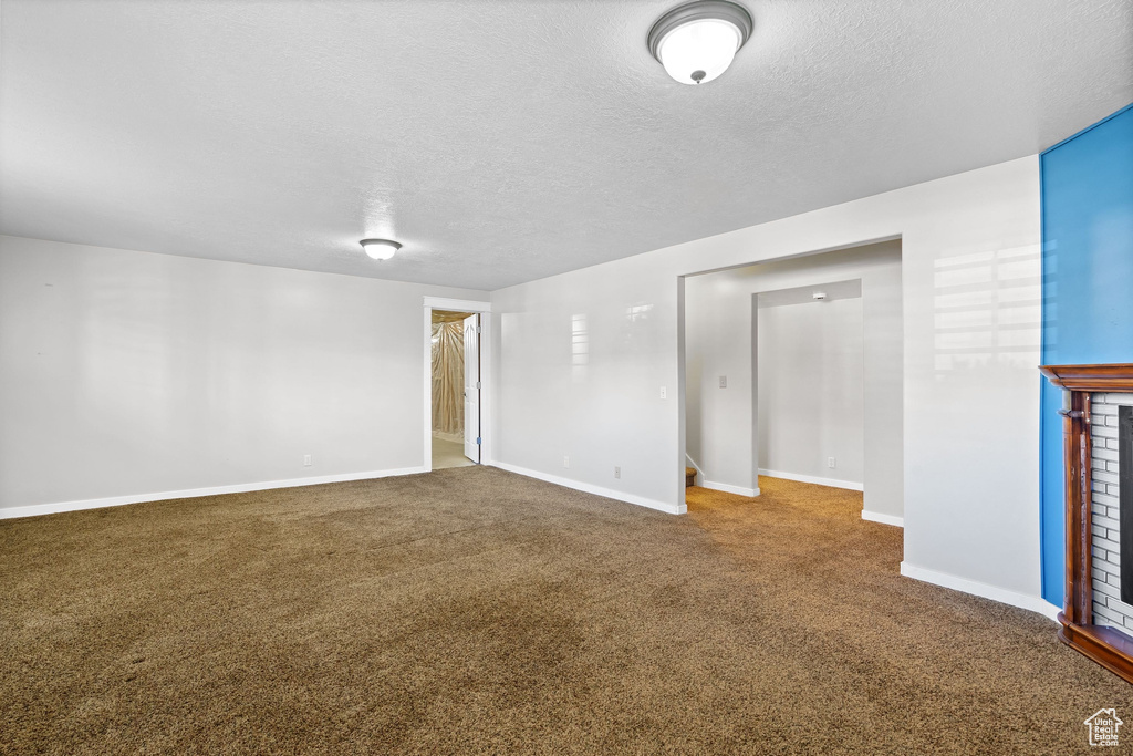 Spare room with carpet, a textured ceiling, baseboards, and a fireplace
