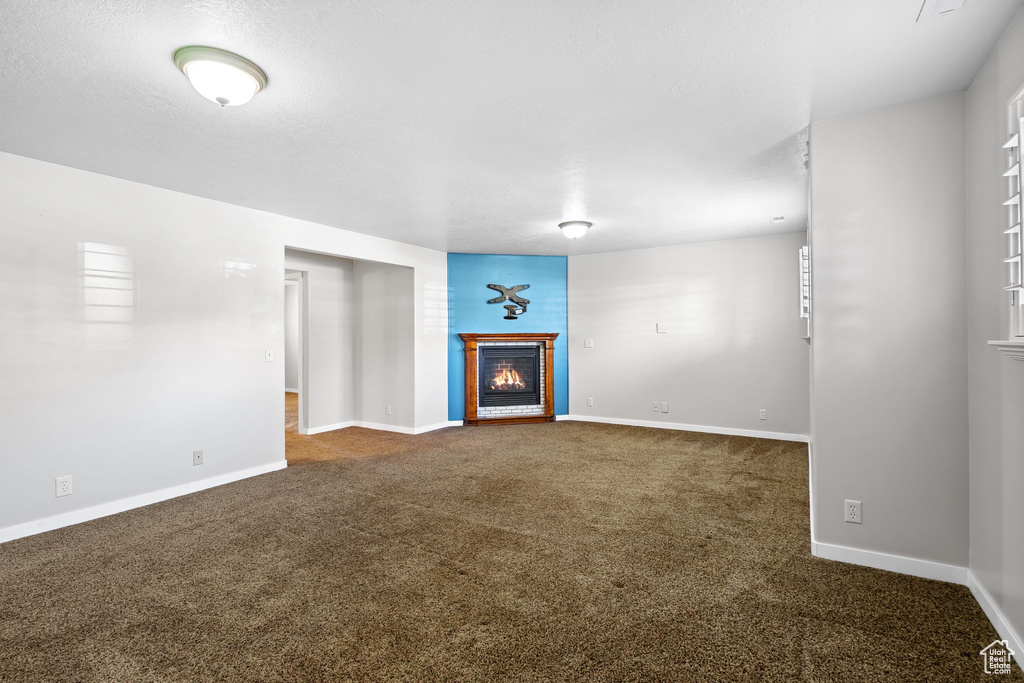 Unfurnished living room featuring a warm lit fireplace, carpet, and baseboards