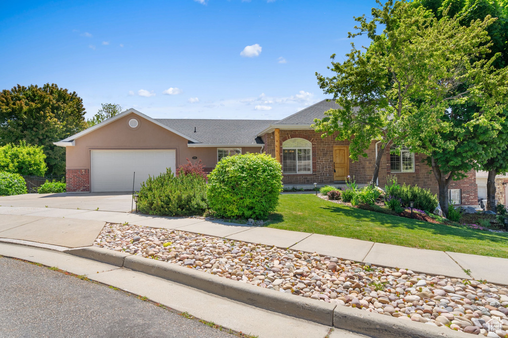 Ranch-style house with brick siding, driveway, an attached garage, a front yard, and roof with shingles