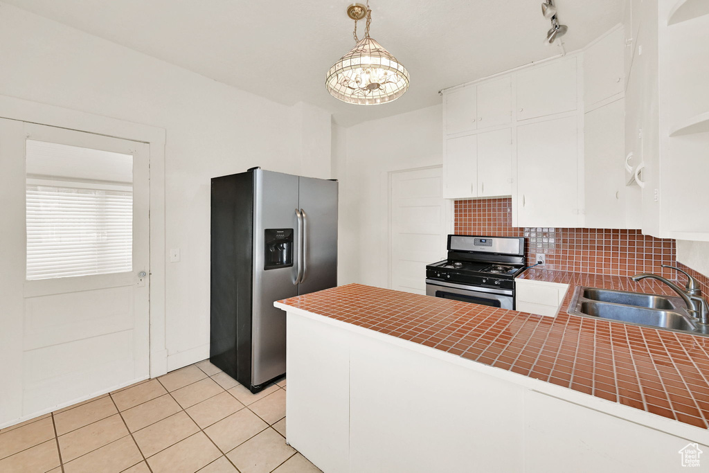 Kitchen with stainless steel appliances, white cabinets, tile countertops, backsplash, and light tile patterned flooring