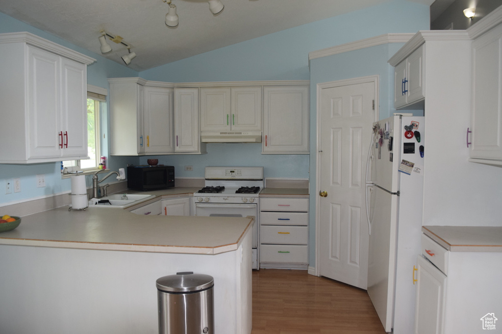 Kitchen with white appliances, under cabinet range hood, a sink, a peninsula, and vaulted ceiling