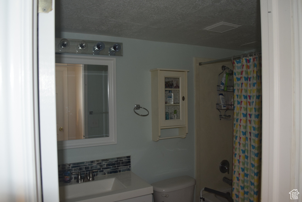 Full bathroom featuring vanity, toilet, a textured ceiling, and shower / bath combo with shower curtain