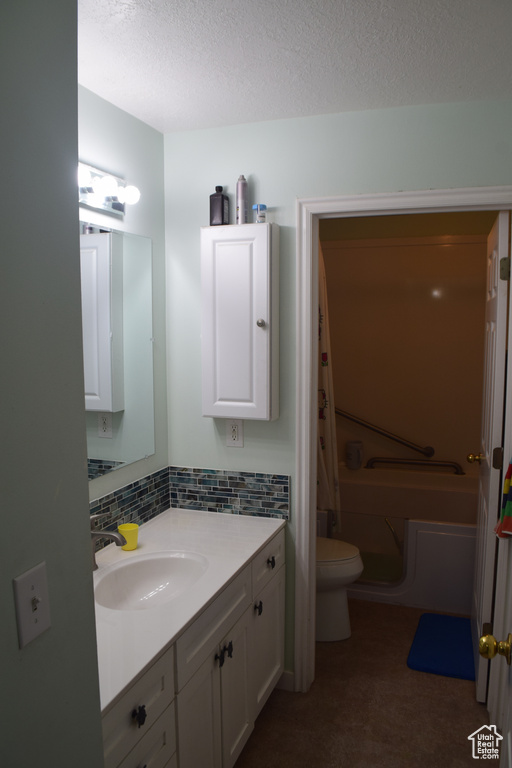 Full bathroom featuring toilet, vanity, a bath, a textured ceiling, and tasteful backsplash