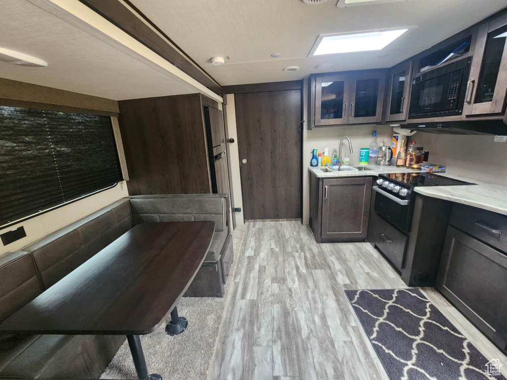 Kitchen with black microwave, light countertops, light wood-style floors, glass insert cabinets, and a sink