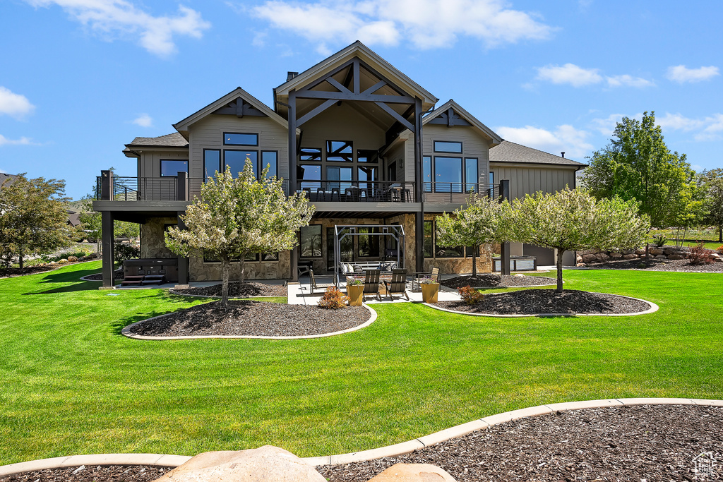Rear view of house with a balcony, a patio area, and a lawn